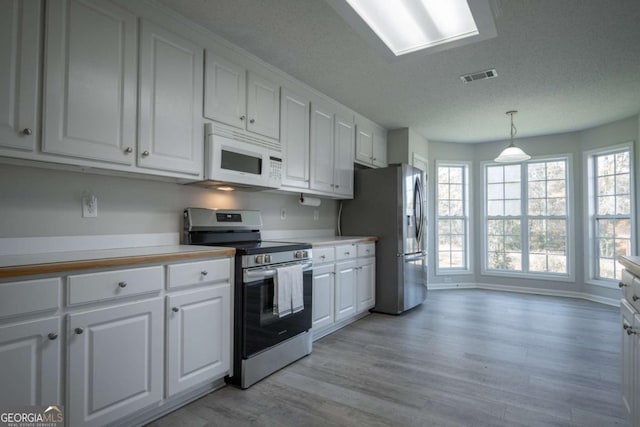 kitchen with white cabinets, light hardwood / wood-style floors, hanging light fixtures, and appliances with stainless steel finishes