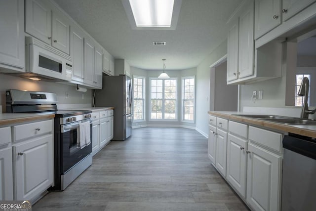 kitchen featuring sink, hanging light fixtures, light hardwood / wood-style flooring, white cabinets, and appliances with stainless steel finishes