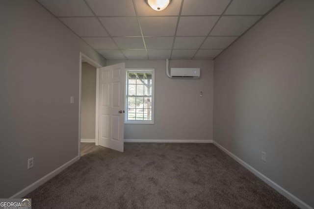 unfurnished room with a wall mounted air conditioner, a drop ceiling, and dark carpet