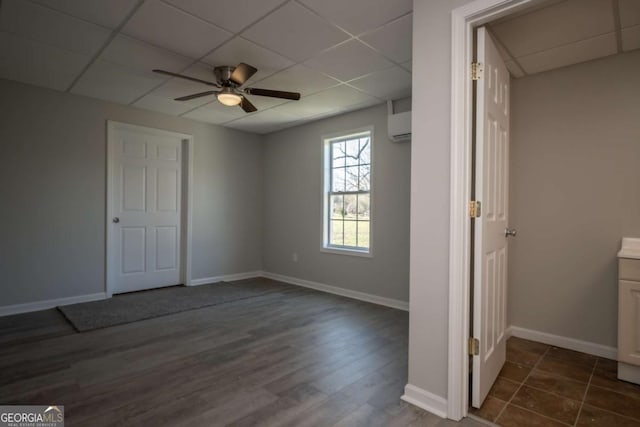 interior space featuring ceiling fan, a drop ceiling, an AC wall unit, and dark wood-type flooring