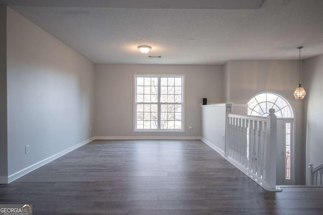 spare room featuring dark wood-type flooring, a textured ceiling, and an inviting chandelier