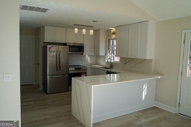 kitchen featuring sink, appliances with stainless steel finishes, tasteful backsplash, white cabinetry, and kitchen peninsula