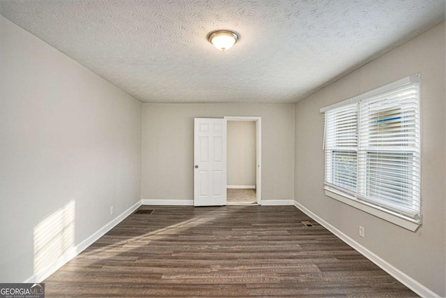 spare room with a textured ceiling and dark wood-type flooring