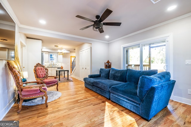 living room featuring ceiling fan with notable chandelier, light hardwood / wood-style floors, and crown molding