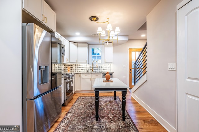 kitchen featuring a notable chandelier, decorative light fixtures, decorative backsplash, white cabinets, and appliances with stainless steel finishes