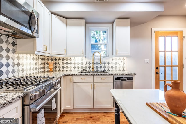 kitchen featuring appliances with stainless steel finishes, white cabinetry, light stone counters, and sink