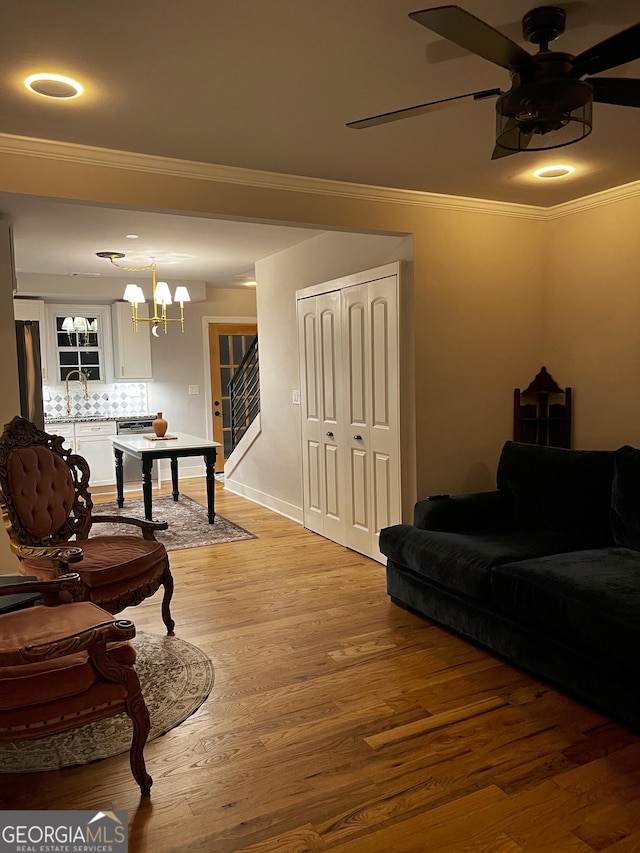 living room featuring ceiling fan with notable chandelier, sink, light wood-type flooring, and ornamental molding