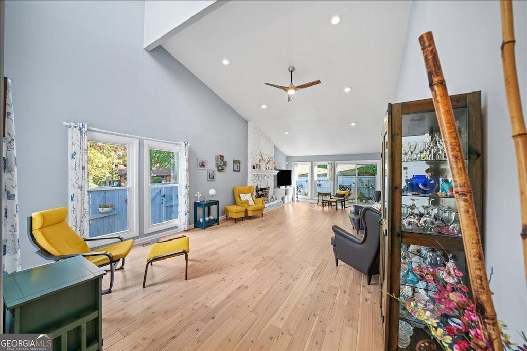 living room with ceiling fan, a stone fireplace, high vaulted ceiling, and light wood-type flooring