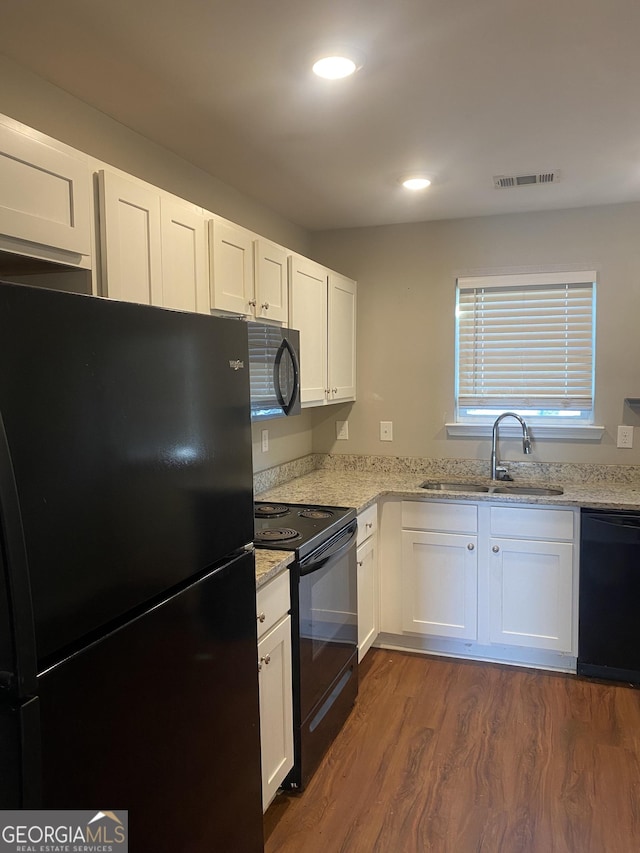 kitchen featuring dark wood-style floors, light stone countertops, black appliances, white cabinetry, and a sink