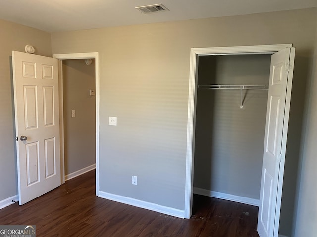 unfurnished bedroom featuring dark wood-style flooring, a closet, visible vents, and baseboards