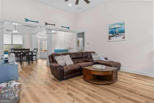 living room featuring light wood-style flooring, recessed lighting, a high ceiling, a ceiling fan, and baseboards