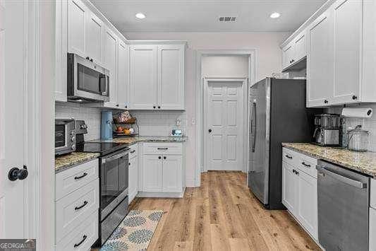 kitchen with light stone countertops, light wood-style flooring, stainless steel appliances, white cabinets, and decorative backsplash