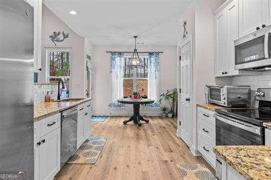 kitchen with light stone counters, light wood finished floors, appliances with stainless steel finishes, white cabinets, and a sink