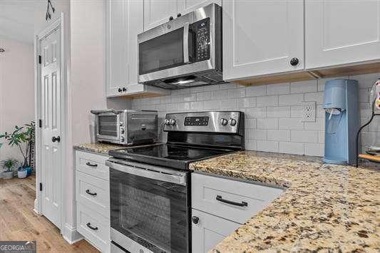 kitchen with appliances with stainless steel finishes, white cabinetry, light wood-style floors, and light stone counters