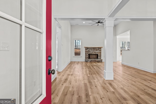 unfurnished living room with ceiling fan, a fireplace, baseboards, light wood finished floors, and ornate columns