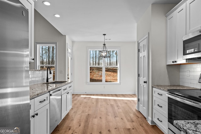 kitchen featuring light stone counters, decorative backsplash, appliances with stainless steel finishes, a sink, and light wood-type flooring