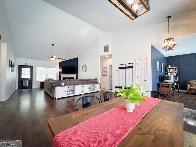 dining space with ceiling fan with notable chandelier, dark wood-type flooring, and high vaulted ceiling