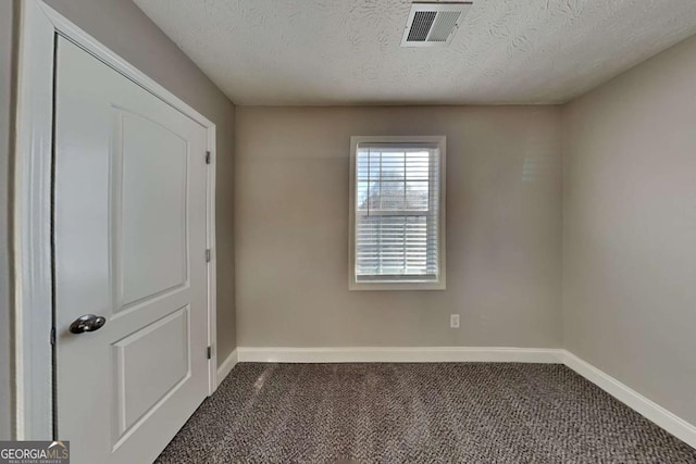 spare room with a textured ceiling and dark colored carpet