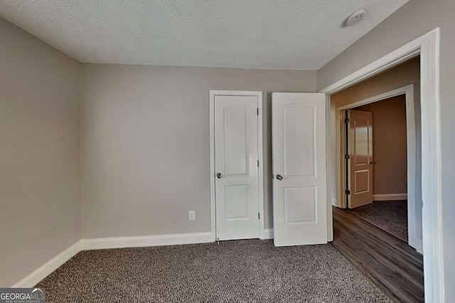 unfurnished bedroom with a textured ceiling and dark colored carpet