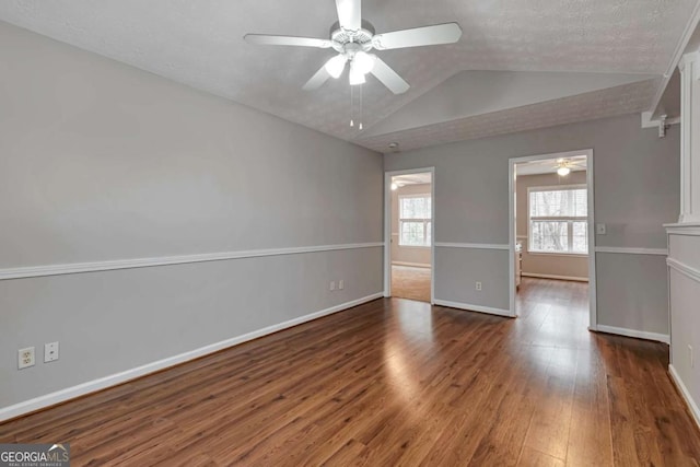 spare room with a textured ceiling, ceiling fan, dark wood-type flooring, and lofted ceiling