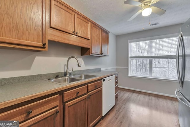 kitchen with light wood-type flooring, white dishwasher, ceiling fan, sink, and stainless steel refrigerator