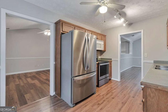 kitchen with a textured ceiling, light hardwood / wood-style floors, stainless steel appliances, and rail lighting