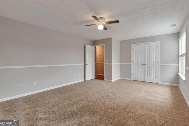 unfurnished bedroom featuring carpet flooring, a textured ceiling, a closet, and ceiling fan