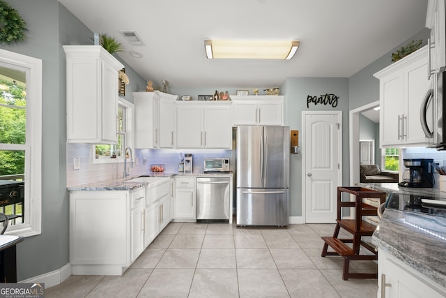 kitchen featuring tasteful backsplash, stainless steel appliances, sink, white cabinets, and light tile patterned flooring