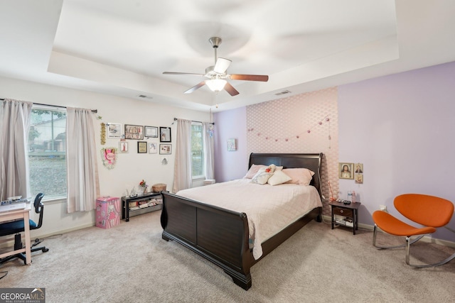 carpeted bedroom with a raised ceiling and ceiling fan