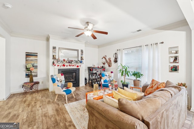 living room with crown molding, ceiling fan, a fireplace, and light hardwood / wood-style floors