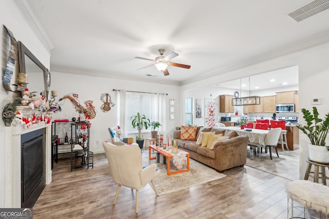 living room featuring light hardwood / wood-style floors, ceiling fan, and crown molding