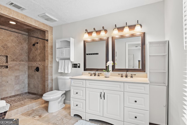 bathroom with vanity, toilet, a tile shower, and a textured ceiling