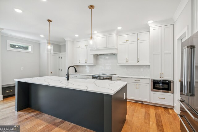 kitchen with pendant lighting, white cabinetry, an island with sink, decorative backsplash, and light stone counters