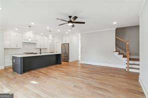 kitchen with ceiling fan, hanging light fixtures, white cabinets, light wood-type flooring, and an island with sink