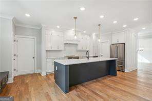 kitchen with high end refrigerator, white cabinetry, hanging light fixtures, and a kitchen island with sink