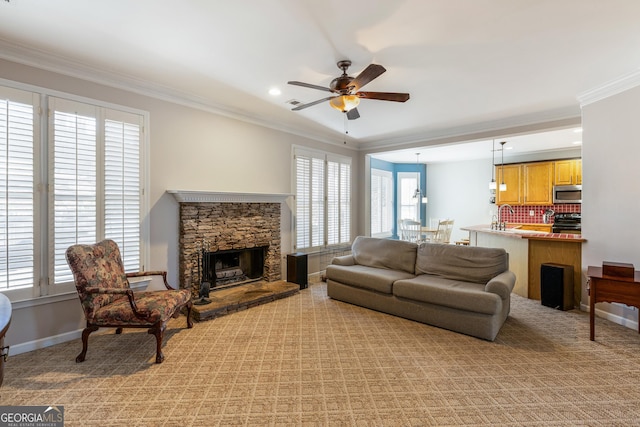 carpeted living room featuring crown molding, ceiling fan, a stone fireplace, and sink