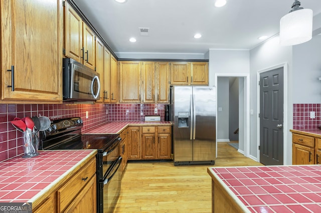 kitchen featuring hanging light fixtures, light wood-type flooring, appliances with stainless steel finishes, tile counters, and decorative backsplash