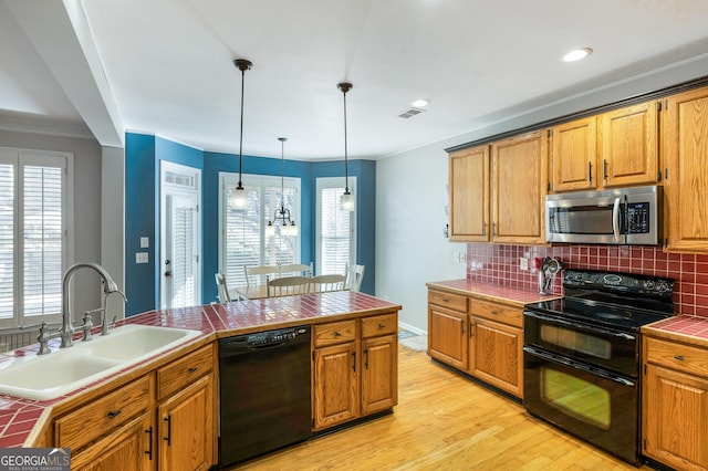 kitchen with sink, tile countertops, hanging light fixtures, light wood-type flooring, and black appliances