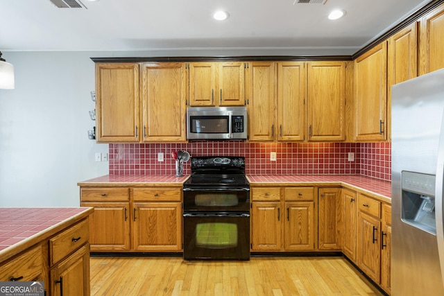 kitchen with decorative backsplash, appliances with stainless steel finishes, tile counters, and light hardwood / wood-style flooring