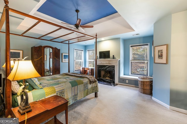 carpeted bedroom with a tray ceiling, a premium fireplace, and ceiling fan