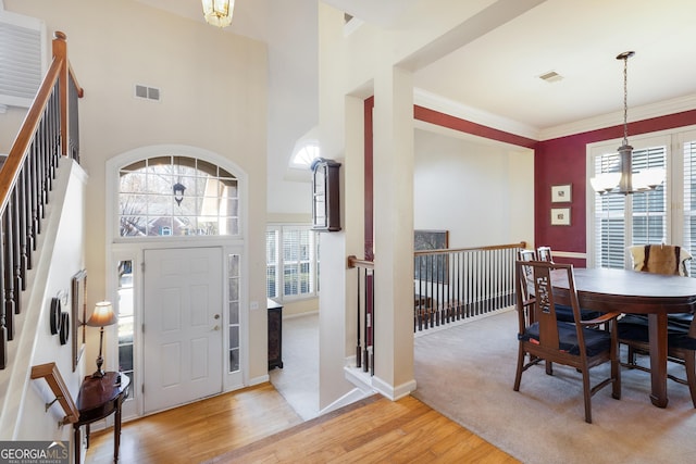 foyer featuring a notable chandelier, crown molding, a towering ceiling, and light wood-type flooring