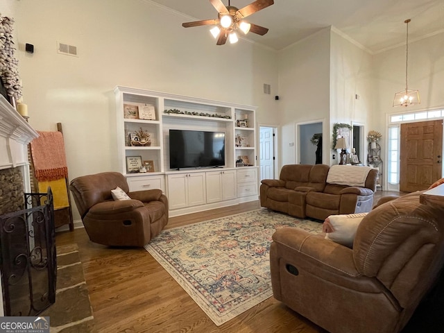 living room with hardwood / wood-style flooring, a stone fireplace, ceiling fan with notable chandelier, and a high ceiling