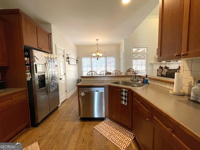 kitchen featuring appliances with stainless steel finishes, sink, hanging light fixtures, kitchen peninsula, and light hardwood / wood-style flooring