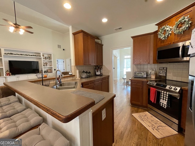 kitchen featuring sink, a kitchen bar, light hardwood / wood-style floors, kitchen peninsula, and stainless steel appliances