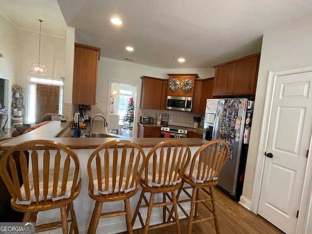 kitchen featuring sink, appliances with stainless steel finishes, kitchen peninsula, hardwood / wood-style floors, and backsplash