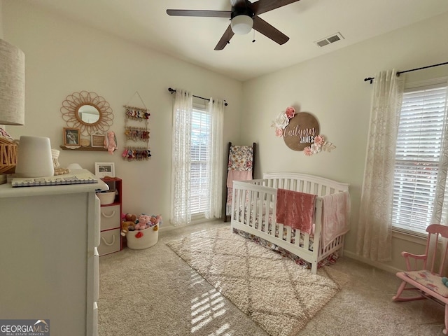 carpeted bedroom featuring ceiling fan and a crib