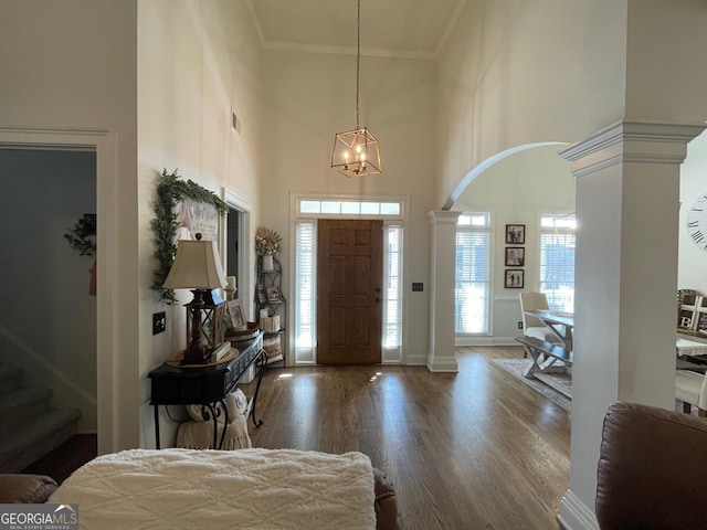 foyer with dark hardwood / wood-style flooring, a towering ceiling, ornamental molding, and ornate columns