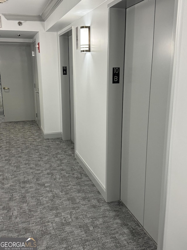 corridor featuring elevator, crown molding, and dark colored carpet