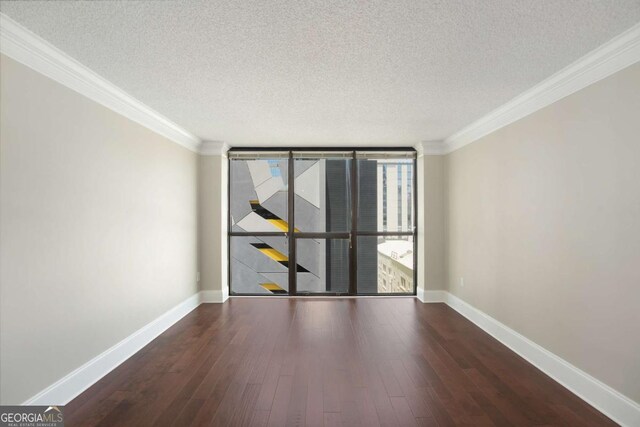 empty room with a textured ceiling, crown molding, a wall of windows, and dark wood-type flooring