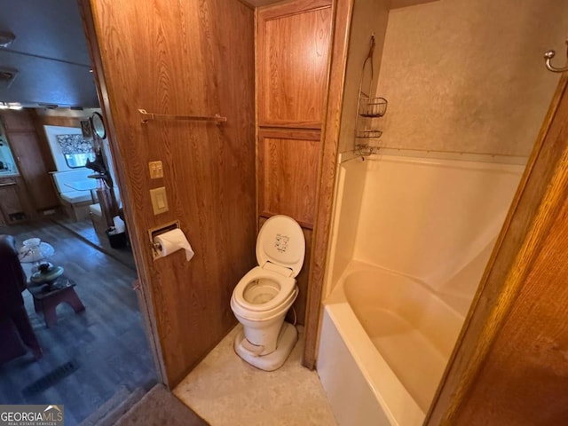 bathroom featuring toilet, shower / washtub combination, and wooden walls